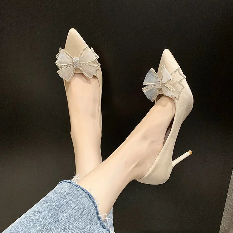 Beige high heels with large sheer bows worn with blue frayed-edge jeans on black background