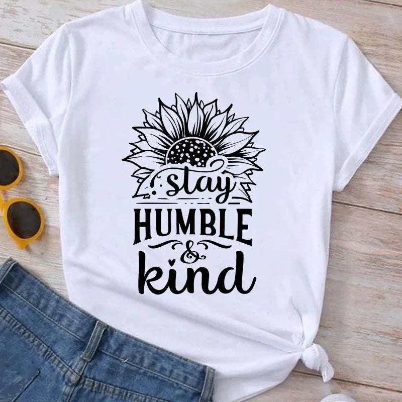 White t-shirt with black sunflower graphic and text 'stay humble & kind' styled with denim shorts and yellow sunglasses