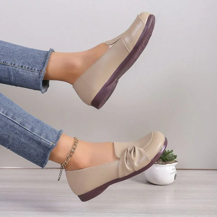 Beige slip-on women's loafers with brown soles, worn with blue jeans and gold anklet, styled with small plant