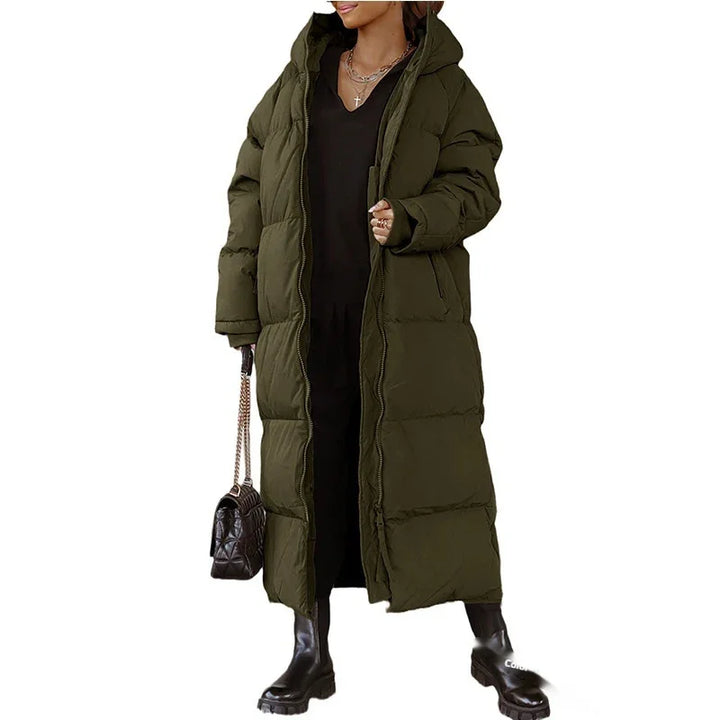 Woman wearing long olive green puffer coat with hood, black outfit, black boots, and black handbag