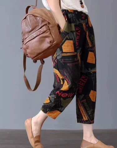 Person wearing black graphic print pants and tan slip-on shoes carrying a brown leather backpack