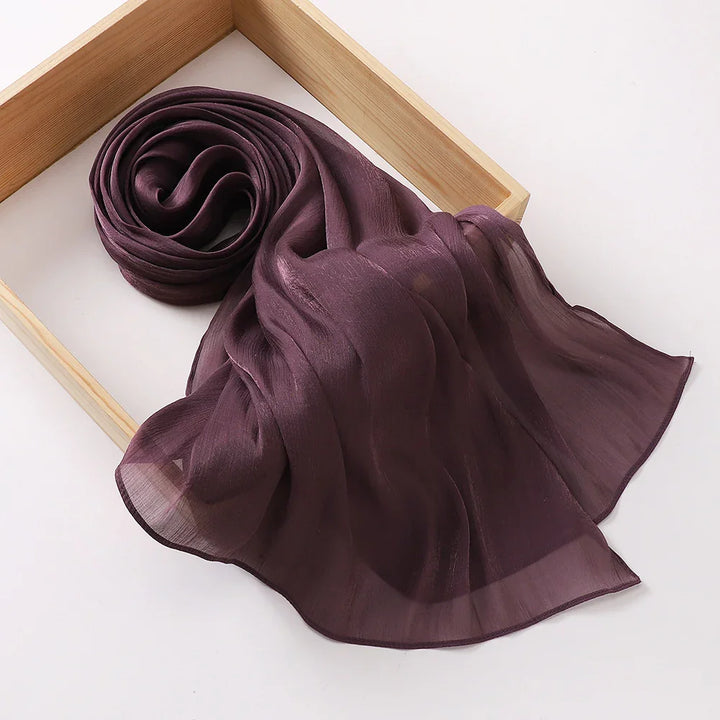 Deep purple sheer chiffon scarf elegantly rolled in a wooden box on white background
