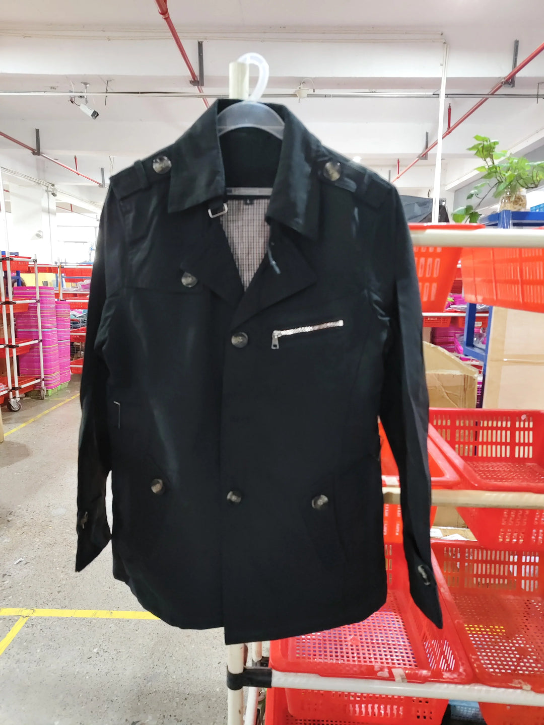 Black double-breasted men's jacket with buttons and zipper pocket, hanging in warehouse