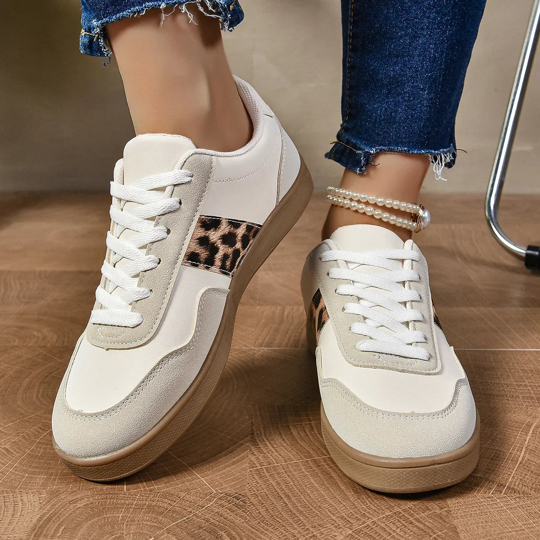 White sneakers with leopard print stripe worn with blue jeans and pearl anklet on wooden floor