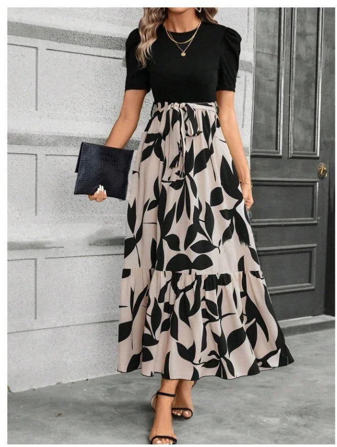 Woman wearing black puff sleeve top and beige skirt with black leaf print holding black clutch