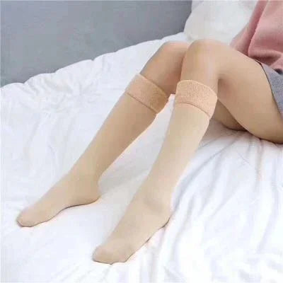 Woman wearing beige knee-high socks sitting on a white bed with gray and pink clothing