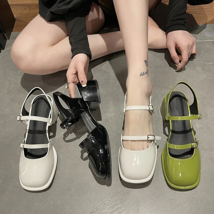 Person trying on white patent leather Mary Jane shoes with black and green pairs on gray floor