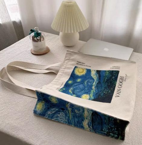 Van Gogh Starry Night canvas tote bag on a desk with lamp, laptop, and glass decor