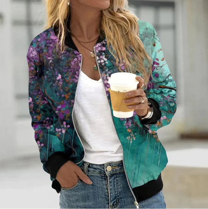 Woman wearing floral print teal bomber jacket with black cuffs, white t-shirt, blue jeans, holding coffee cup