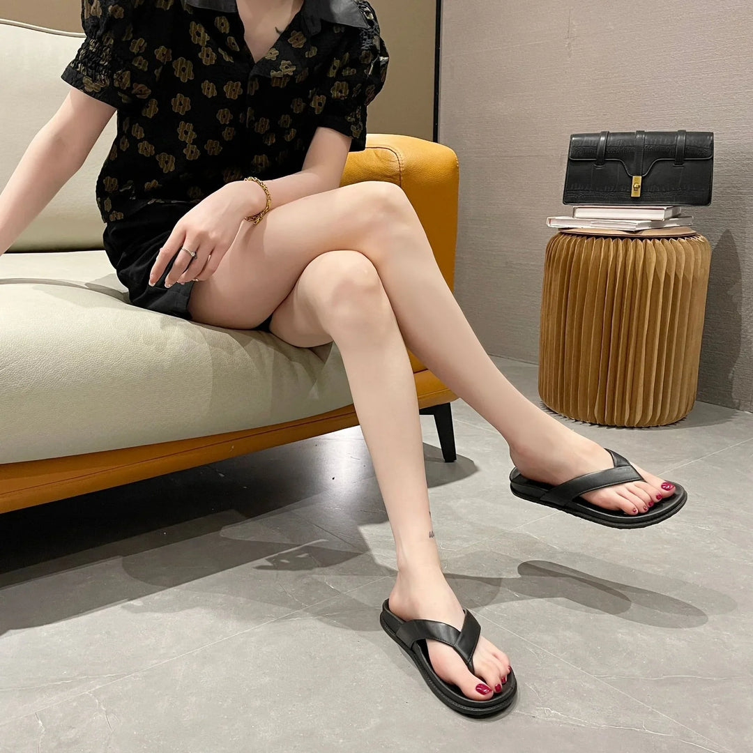 Woman in black floral dress sitting on sofa wearing black leather flip-flop sandals indoors