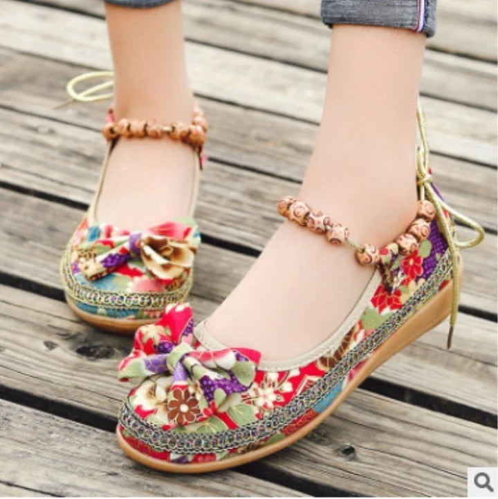 Close-up of colorful floral fabric shoes with bows and wooden bead ankle bracelets on wooden floor