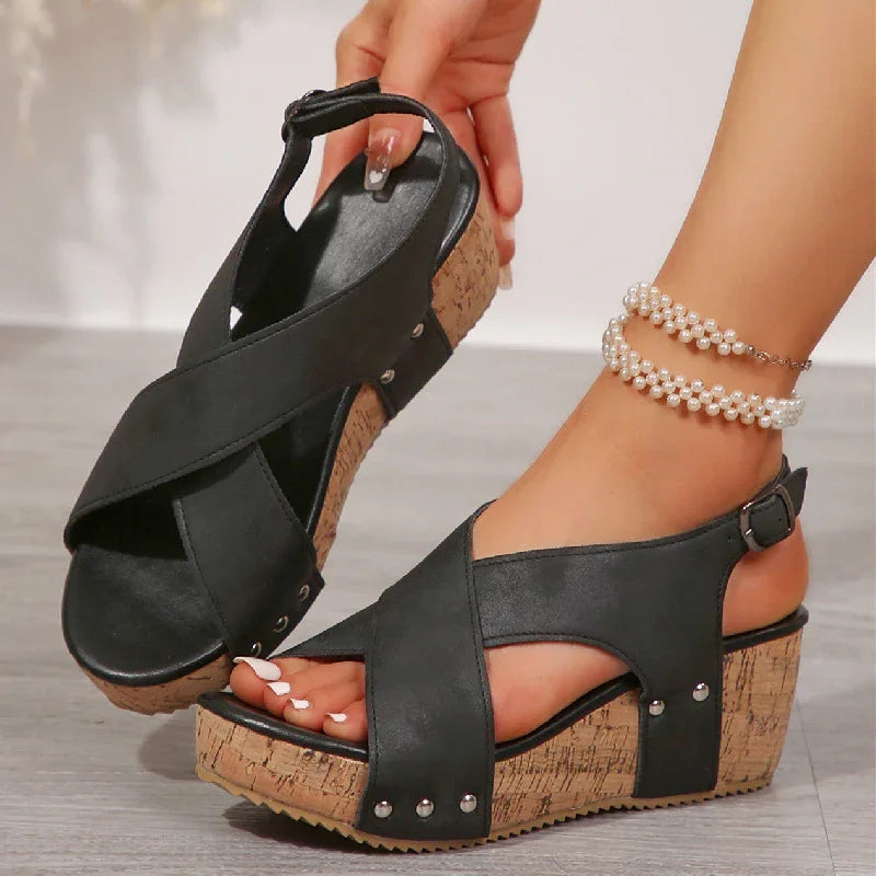 black wedge sandals with cork heels and silver studs worn with pearl anklets on wooden floor