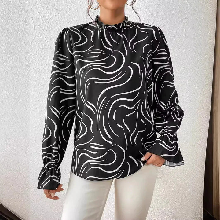 Woman wearing black blouse with white abstract wave pattern and long sleeves, paired with white pants