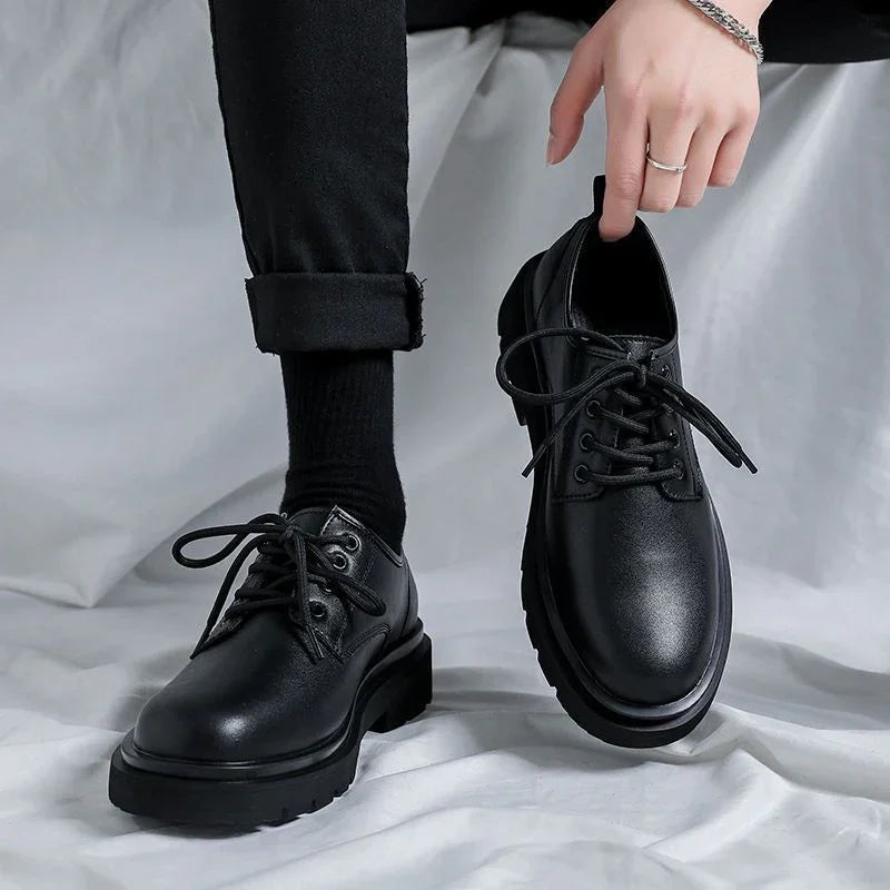 Stylish black leather lace-up shoes worn with black socks and pants, held by a hand with silver rings and bracelet