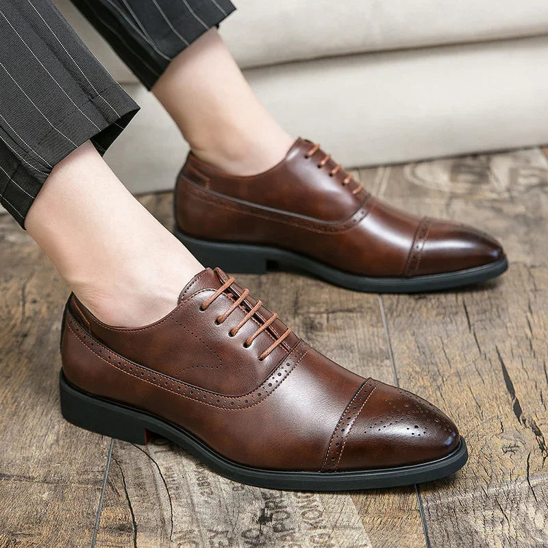 Men's brown leather dress shoes with brogue detailing worn with pinstriped trousers on wooden floor