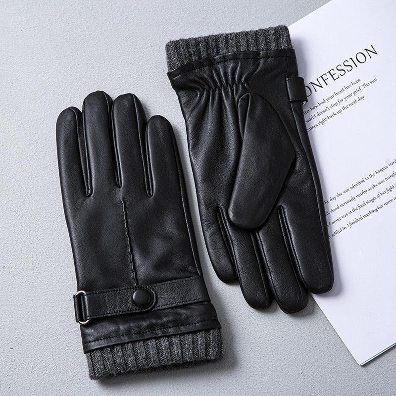 Black leather winter gloves with gray knit cuffs and button strap on a gray surface next to a white paper