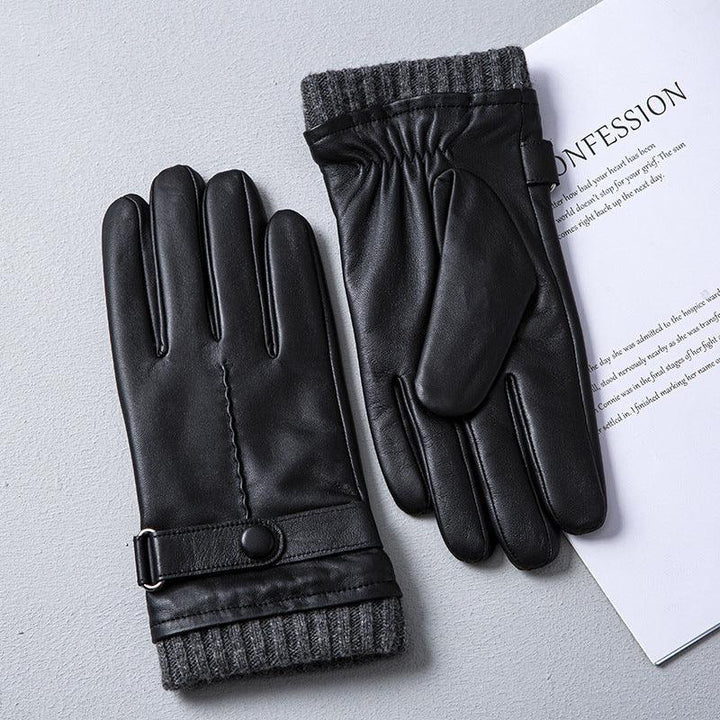 Black leather winter gloves with gray knit cuffs and button strap on a gray surface next to a white paper