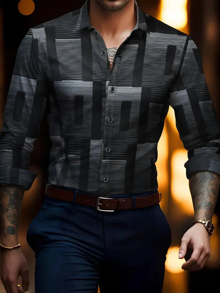 Man wearing a black and grey geometric patterned button-up shirt with rolled sleeves, paired with dark pants and a brown belt