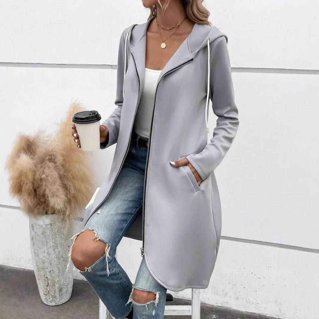 Woman wearing long light gray zip-up hoodie with hood and pockets, paired with ripped jeans, holding coffee cup