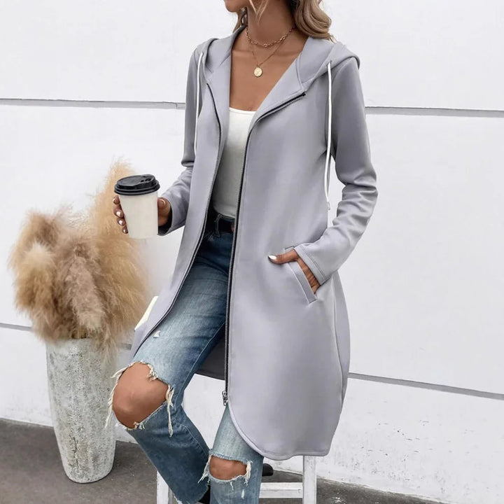 Woman wearing long light gray zip-up hoodie with hood and pockets, paired with ripped jeans, holding coffee cup