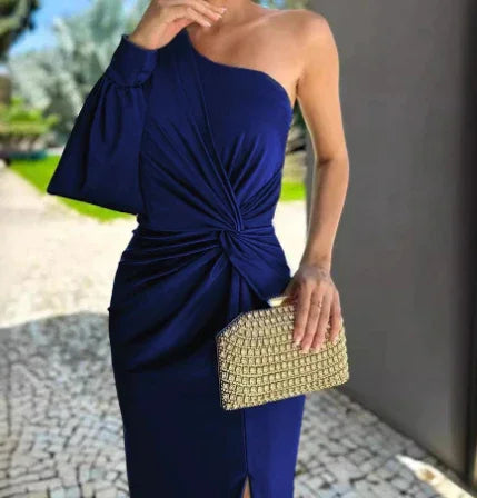 Woman wearing navy blue one-shoulder dress with gathered waist detail holding gold clutch outdoors