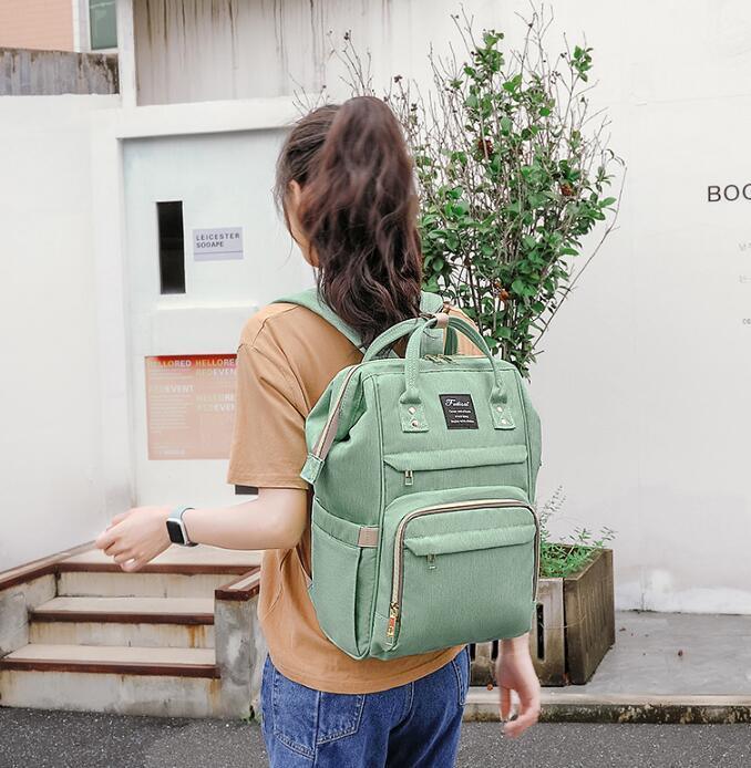 Woman wearing brown shirt and blue jeans carrying green backpack outdoors near a plant and stairs