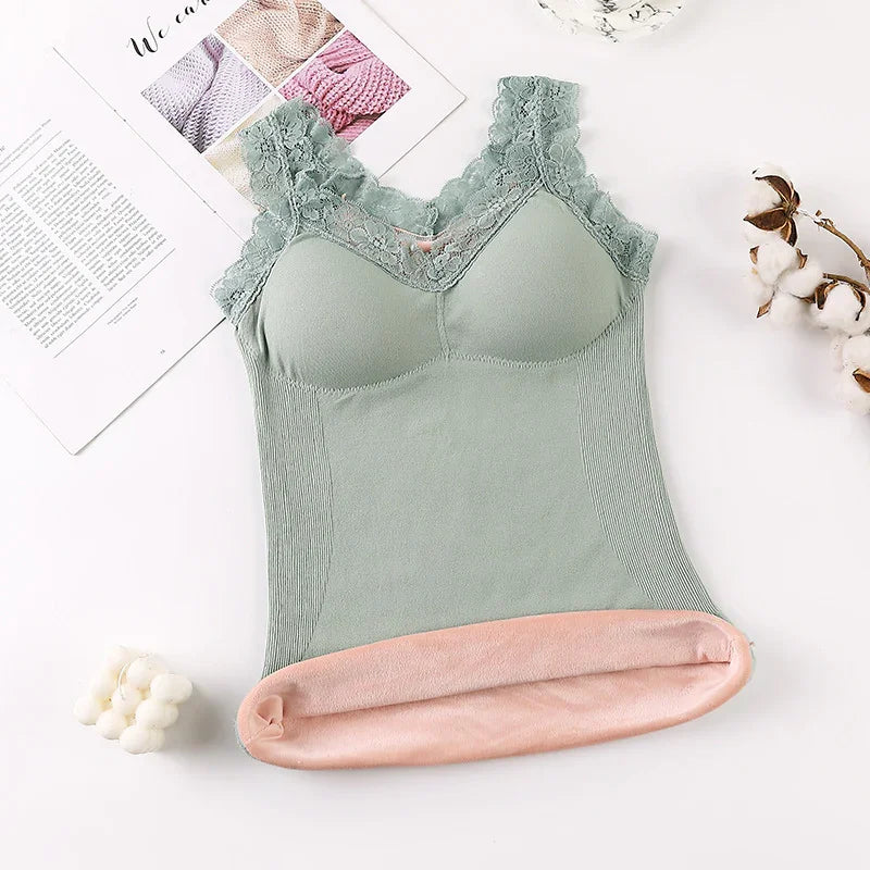 Green lace-trimmed padded camisole with soft pink fleece lining on white background with cotton sprigs and magazine