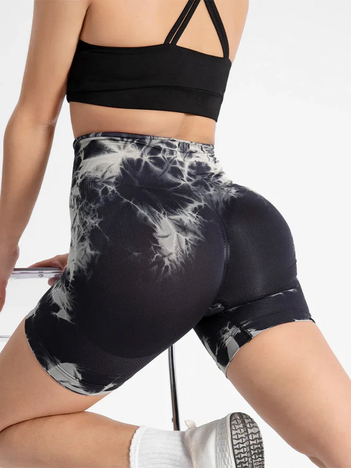 Woman wearing black and white tie-dye biker shorts and black sports bra in athletic pose