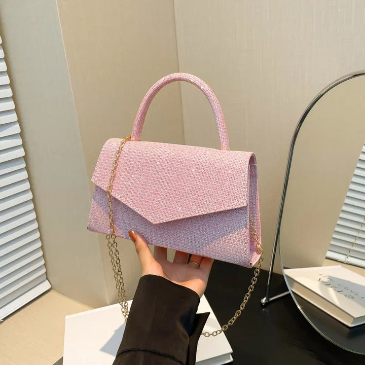 Hand holding a pink textured handbag with gold chain strap in a modern room
