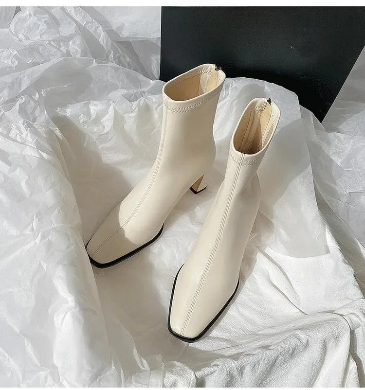 Cream white square-toe ankle boots with mid heels on crumpled white fabric background