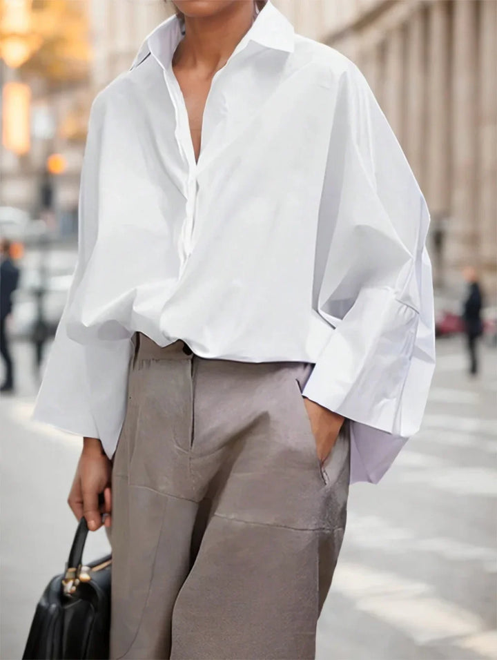 Person wearing oversized white shirt and gray pants, holding black handbag on city street