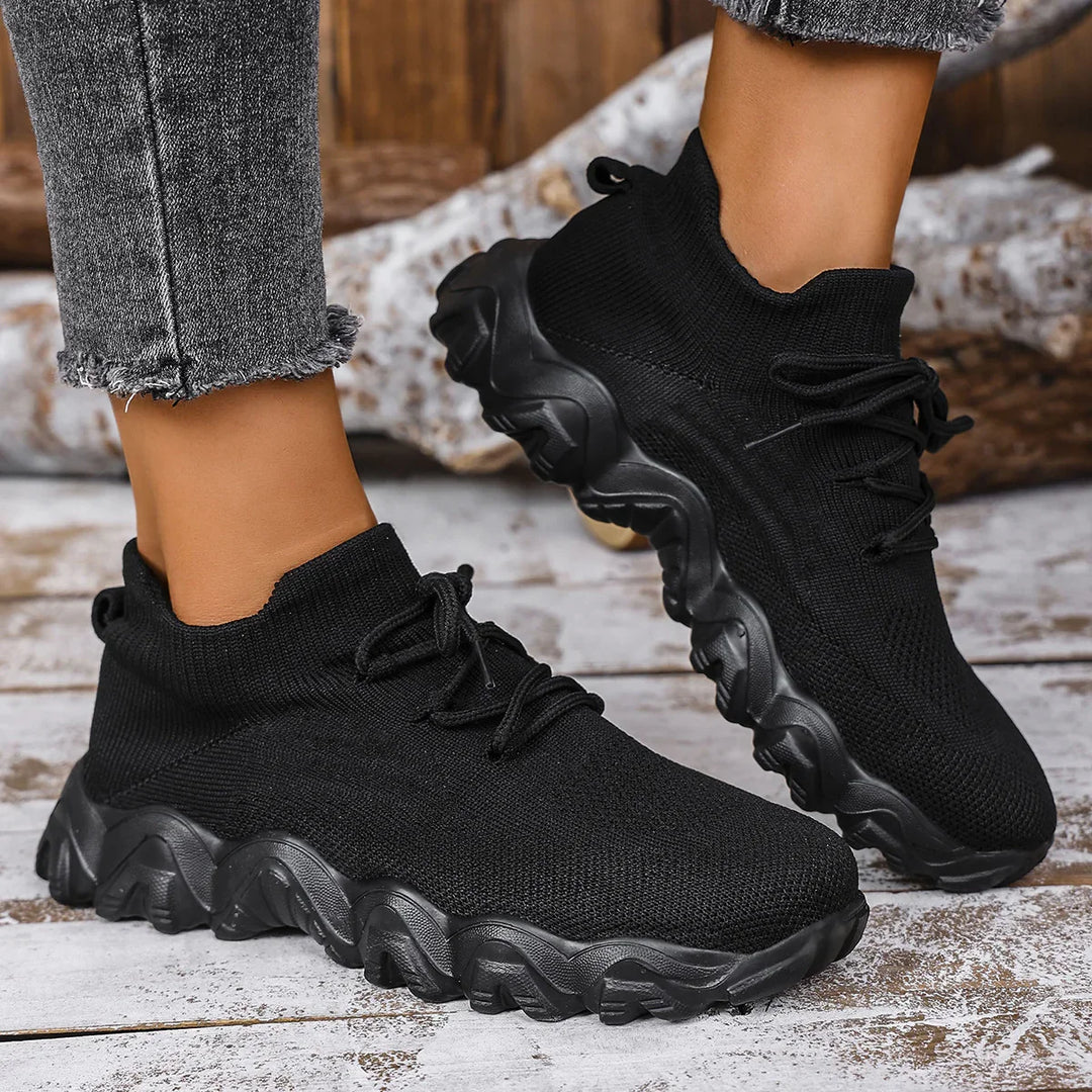 Black knitted sock sneakers with chunky sole worn with frayed gray jeans on wooden floor