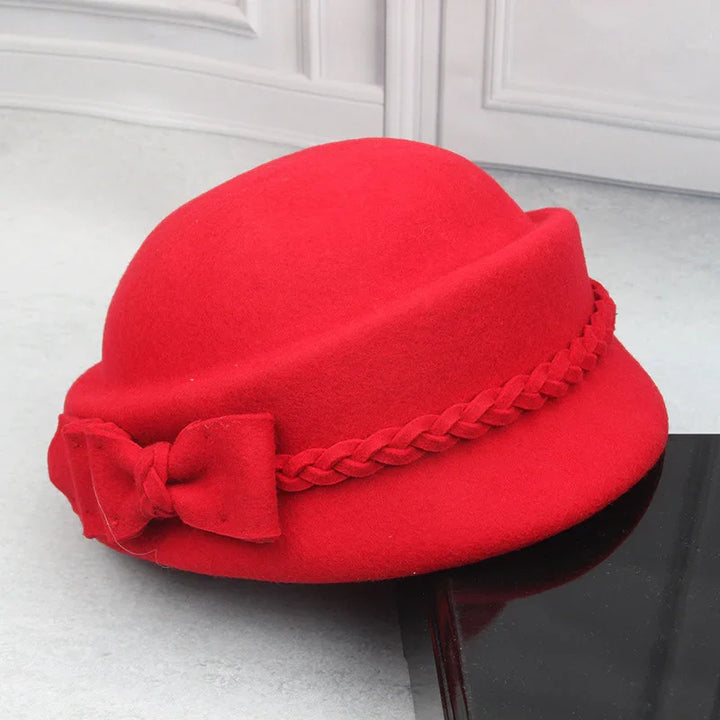 Red vintage-style felt cloche hat with braided band and bow detail on white surface