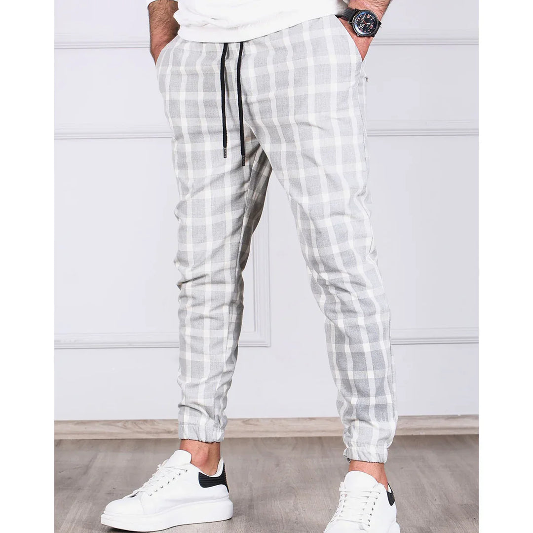 Men's gray and white checkered jogger pants with black drawstrings worn with white sneakers