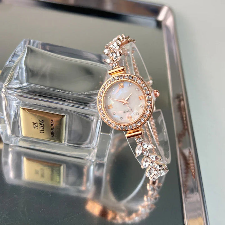 Elegant rose gold women's quartz watch with crystal-studded bezel and leaf design bracelet on reflective surface