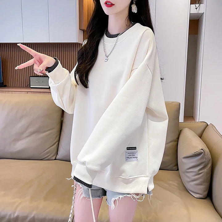 Woman wearing oversized white sweatshirt with label, paired with ripped denim shorts indoors