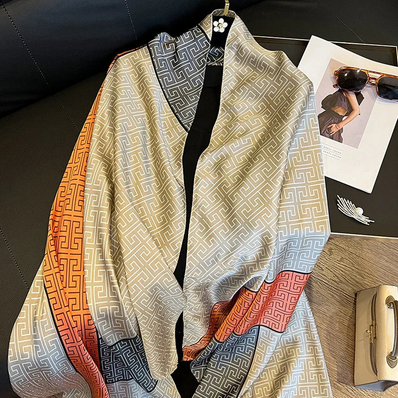 Silk scarf with geometric pattern in orange, beige, navy, and pink laid on black surface beside sunglasses, magazine, and white handbag