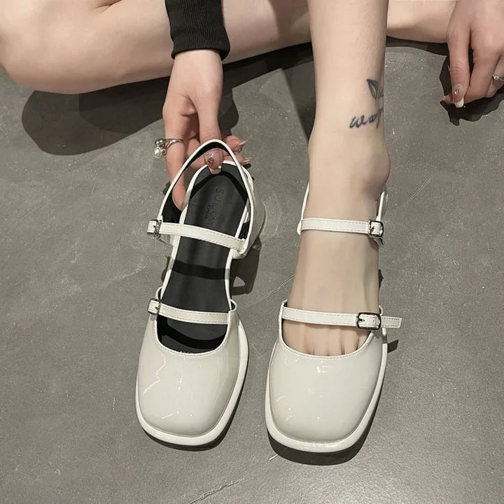 Person wearing white patent leather square-toe Mary Jane shoes with double straps on concrete floor