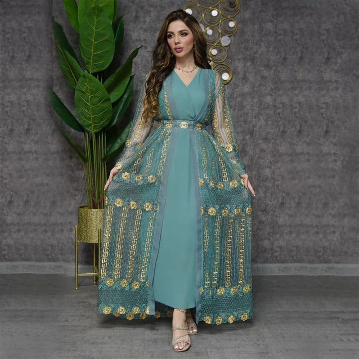 Elegant woman in teal dress with gold embroidered sheer overlay posing indoors by plant and wall art