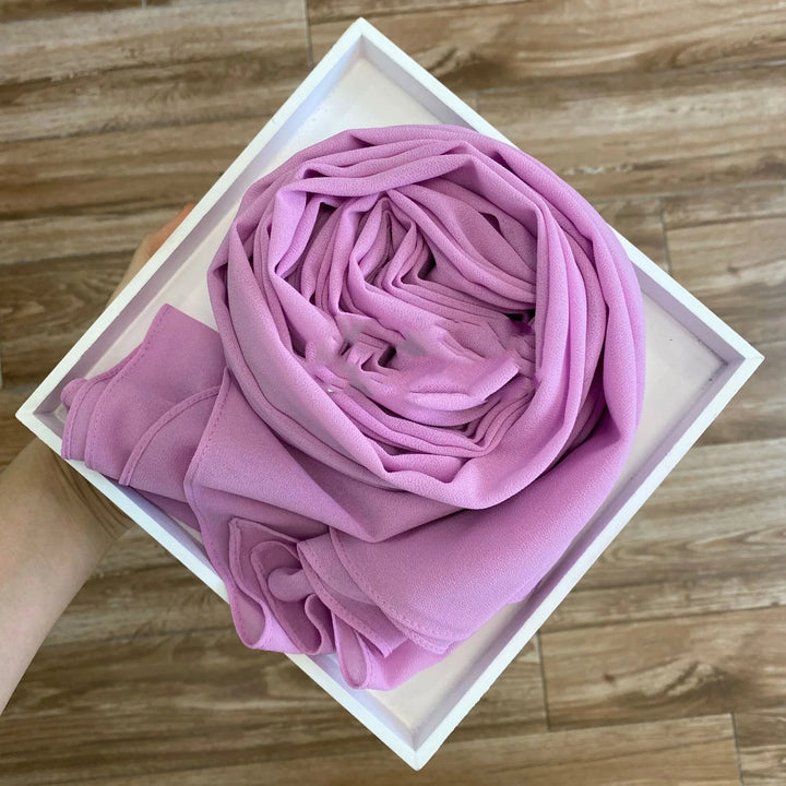 Hand holding white square box with neatly folded pink fabric inside on wooden floor