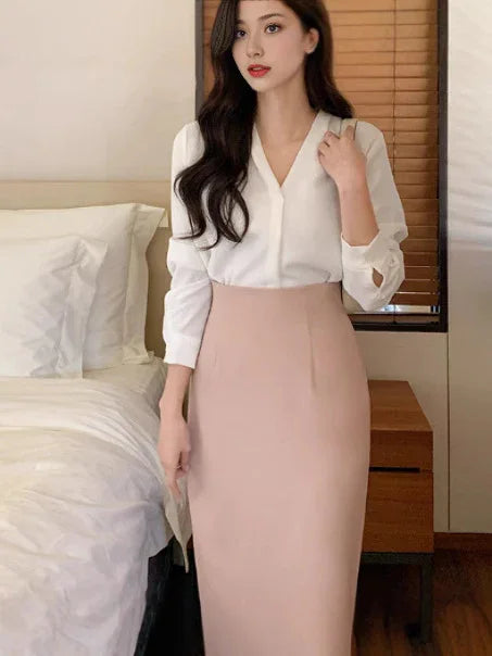 Woman wearing white V-neck blouse and high-waisted beige pencil skirt in bedroom with white bed