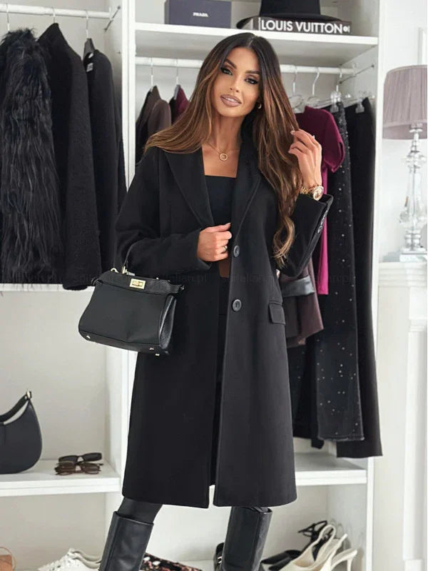 Fashionable woman in a black long coat, black boots, holding a black handbag in a stylish closet