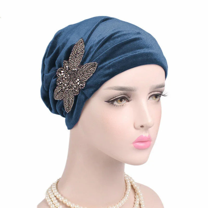 Mannequin wearing blue turban with beaded floral brooch and pearl necklace on white background