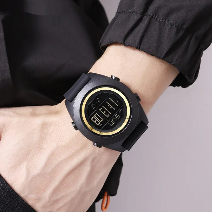 Close-up of a black digital wristwatch with a gold ring on a person's wrist wearing a black jacket