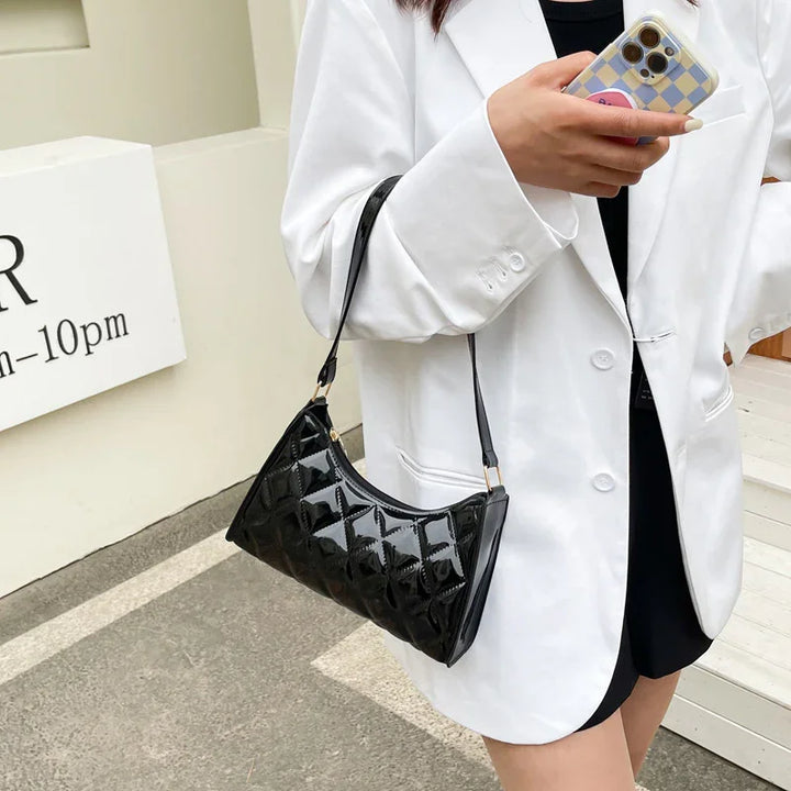 Woman in white blazer holding a black patent leather handbag and phone with checkered case