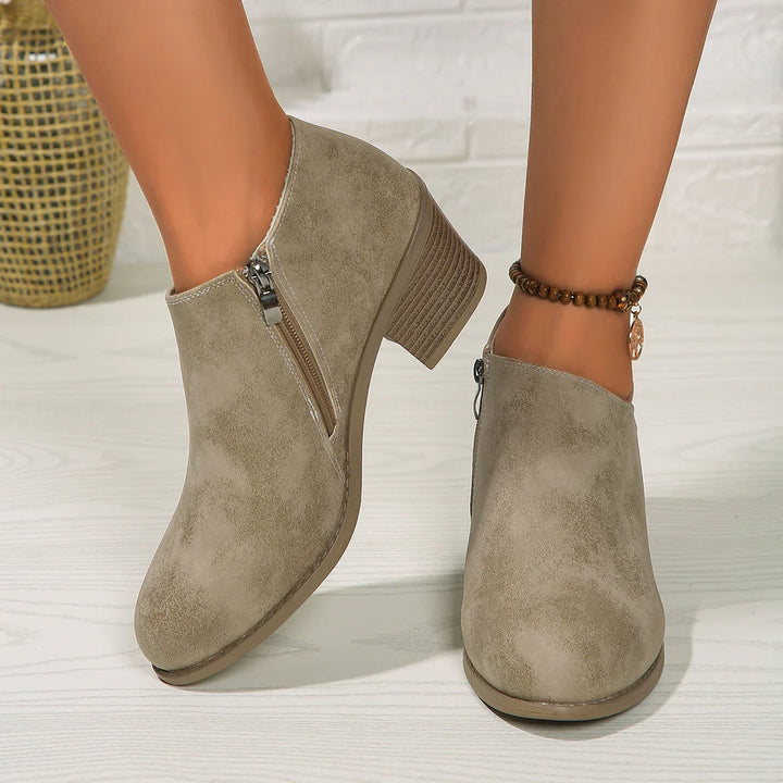Women's taupe suede ankle boots with side zipper and low stacked heel on light wood floor