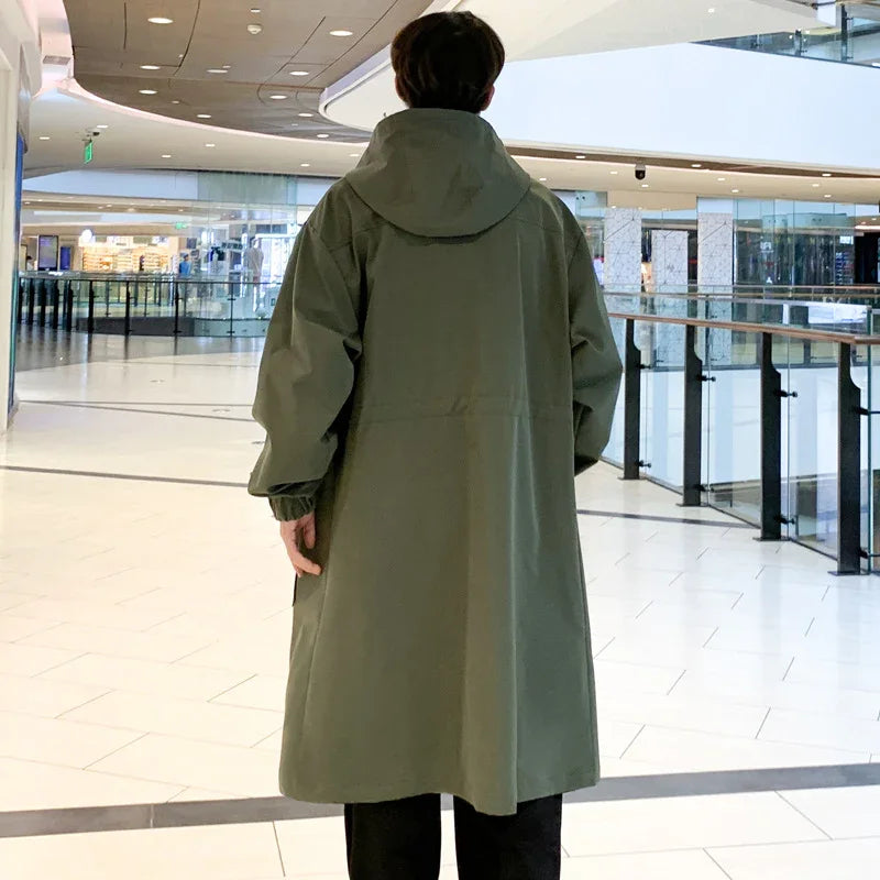 Man wearing long olive green hooded coat standing in modern shopping mall interior