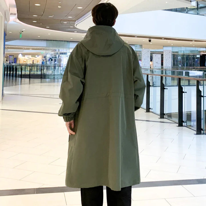 Man wearing long olive green hooded coat standing in modern shopping mall interior