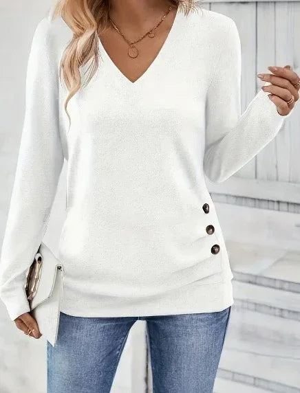 Woman wearing white V-neck long sleeve sweater with side buttons and blue jeans holding a white clutch