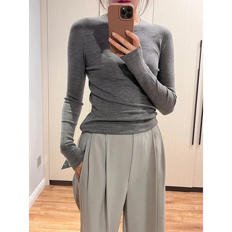 Person wearing fitted grey long-sleeve sweater and light beige pleated trousers taking mirror selfie